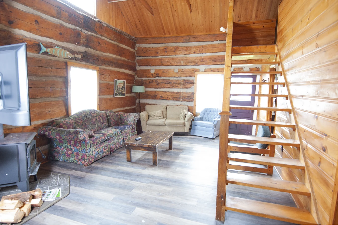 Pigeon Lake Resort Cottage Seven.&nbsp; Log cabin living room with sofas, wood stove, and staircase to loft.